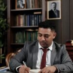 A professional lawyer in a suit sits at a wooden desk in a well-decorated office.