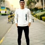 Smiling young man posing confidently on a city street during the day.